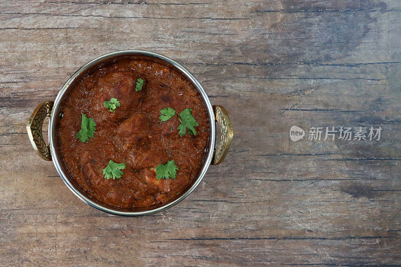 木桌的形象是卡扎伊(kadhai)烹饪锅/盛满自制鸡肉布娜(bhuna)的碗，绿色香菜叶装饰，木纹背景copyspace，抬高的视野